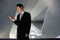 Businessman standing in tunnel, looking at mobile phone - Yukmin