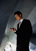Businessman in tunnel, looking at mobile phone - Yukmin