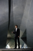 Businessman standing in tunnel, holding mobile phone, smiling at camera - Yukmin