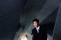 Businessman in tunnel, looking at mobile phone - Yukmin