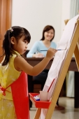 Young girl painting on easel, mother in the background - Alex Mares-Manton