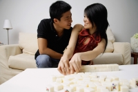 Couple looking at each other, mahjong tiles on the table in front of them - Alex Mares-Manton