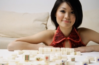 Young woman looking at camera, mahjong tiles on table in front of her - Alex Mares-Manton