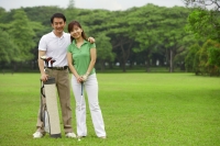 Couple with golf club and golf bag on golf course, smiling at camera - Alex Mares-Manton