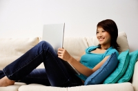 Woman reclining on sofa, using laptop - Nugene Chiang