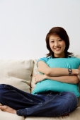 Woman sitting on sofa, hugging cushion, looking at camera - Nugene Chiang
