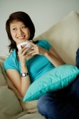 Woman sitting on sofa, holding mug, looking away - Nugene Chiang