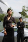 Woman in foreground, with hand on hip, man in background, leaning on car - Alex Mares-Manton