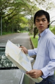 Man standing next to car, holding map, looking over shoulder - Alex Mares-Manton