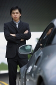 Businessman with arms crossed, standing next to car, portrait - Alex Mares-Manton