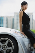 Woman leaning on hood of car, looking at camera, portrait - Alex Mares-Manton