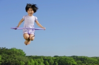 Girl jumping in mid air, holding plastic hoop - Alex Mares-Manton