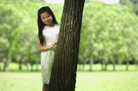Girl standing behind tree trunk, smiling at camera - Alex Mares-Manton