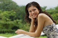 Young woman leaning on railing, hand on chin, smiling at camera - Yukmin