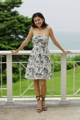 Young woman in floral dress, standing on balcony, smiling at camera - Yukmin