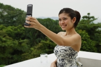 Young woman in floral dress, standing on balcony, using mobile phone to take a picture - Yukmin