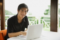 Man in cafe using laptop, smiling at camera - Yukmin