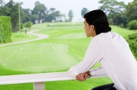 Man leaning on railing, looking out at golf course - Yukmin