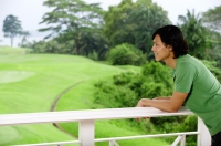 Man leaning on railing, looking out at golf course - Yukmin