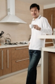 Man standing in kitchen, holding cup, looking at camera - blueduck