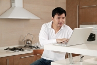 Man in kitchen, using laptop - blueduck