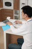 Man sitting at kitchen counter with calculator and bills - blueduck