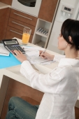 Woman sitting at kitchen counter with calculator and bills - blueduck