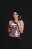 Woman standing against black background, holding bowl - Yukmin