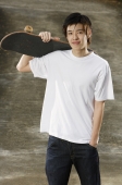Young man holding skateboard over shoulder - Yukmin