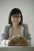 Young woman smiling at camera, open book in front of her - Yukmin