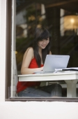 Young woman sitting at table, using laptop - Yukmin