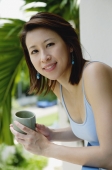 Woman leaning on railing, holding cup, looking at camera - Yukmin