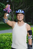 Mature adult wearing helmet, holding up medal - Yukmin