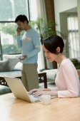 Couple at home, woman using laptop, man in the background on the phone - blueduck