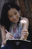 Young woman holding flower, writing in notebook - Yukmin