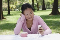 Young woman sitting at outdoor table, listening to MP3 player - Yukmin