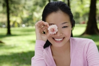 Young woman holding flower over eye - Yukmin