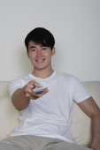 Young man, pointing TV remote control towards camera - Yukmin