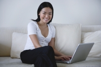 Woman sitting on sofa, using laptop, smiling at camera - Yukmin