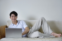 Man lying on sofa with laptop - Yukmin