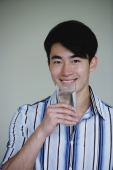 Young man holding glass of water, smiling - Yukmin