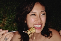 Woman holding fork full of pasta, smiling - Yukmin