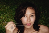 woman holding chopsticks up to mouth, looking out of corner of eye - Yukmin