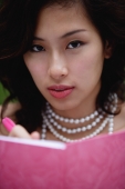 Woman wearing necklace and writing in pink journal, looking at camera - Yukmin