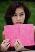 Woman sitting in cafe holding pink journal and pink pen, looking away from camera - Yukmin