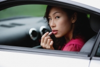 Woman sitting in car, applying lipstick, looking over shoulder out window - Yukmin