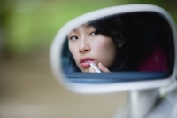 Woman applying lipstick in side view mirror of car - Yukmin