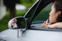 Woman applying lipstick in side view mirror of car, while in driver's seat - Yukmin