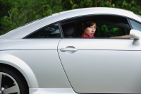 Woman driving car, looking out window at camera - Yukmin