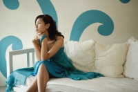 Woman sitting on daybed, looking away from camera - Yukmin